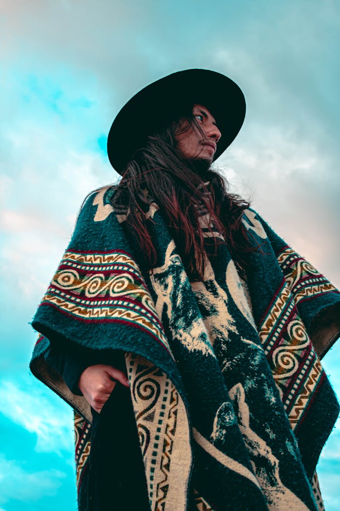 Low angle view of a person in a traditional Andean poncho and hat against a cloudy sky in Quito.