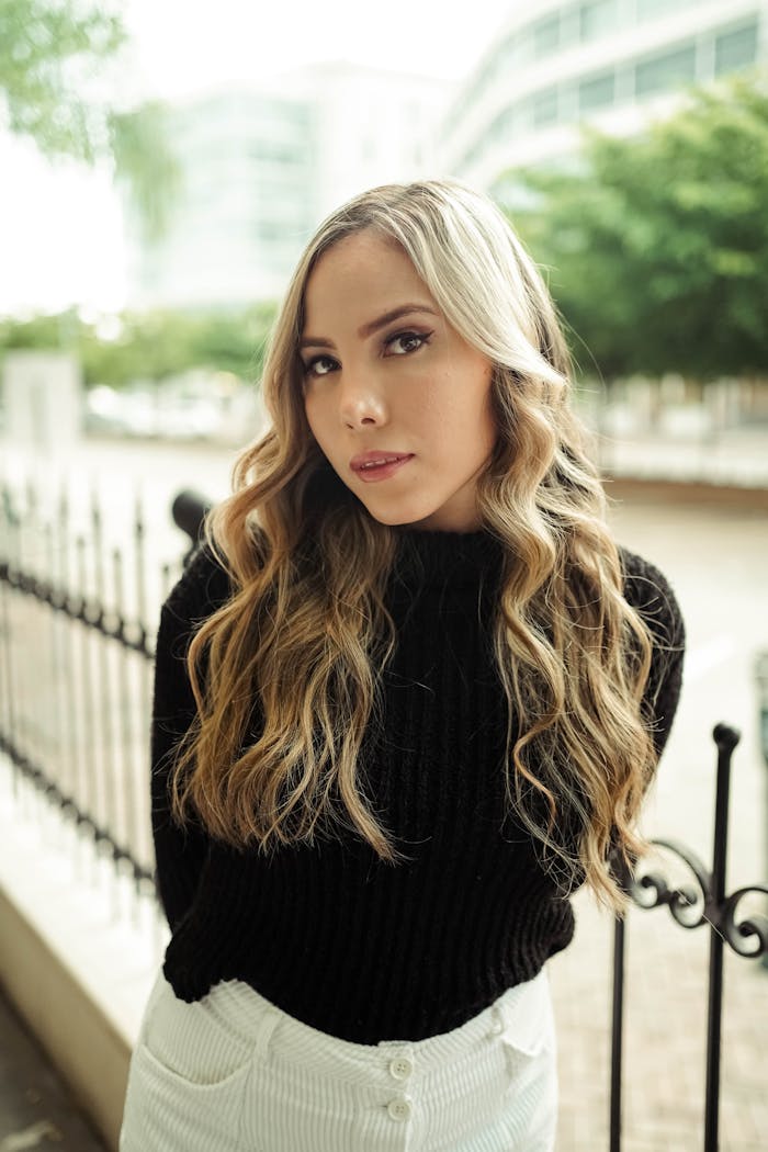 Elegant woman with wavy blonde hair and black sweater poses outdoors in Samborondón, Ecuador.