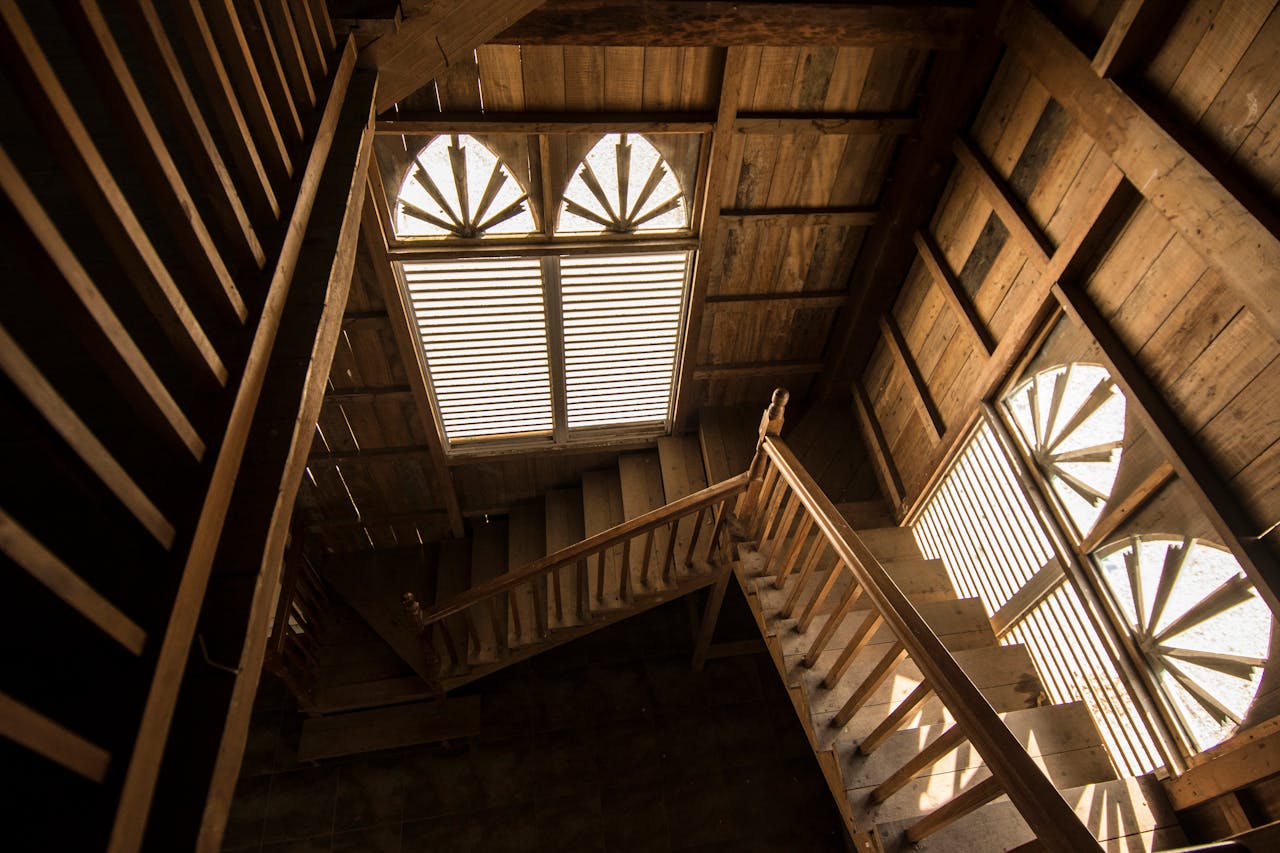 Rustic wooden staircase with sunlit windows casting intricate shadows, creating a warm and inviting atmosphere.